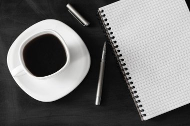 Siyah yüzeye yakın beyaz kahve, metal kalem ve not defteri.