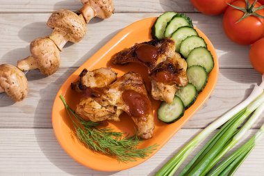 Ahşap arka planda sebzeli ve otlu kızarmış tavuk kanadı tabağı. Yakın plan.