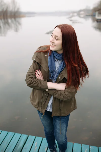 Женщина, стоящая на пирсе у реки в холодный облачный день и улыбающаяся — стоковое фото