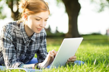 Genç kadın parkta çim üzerinde yalan ve dijital tablet kullanma