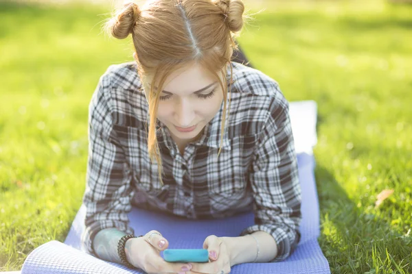 Young woman lying on grass in park and using smartphone — Stock Photo, Image