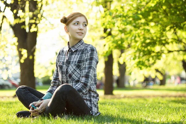 公園で草の上に座っている若い女性は — ストック写真