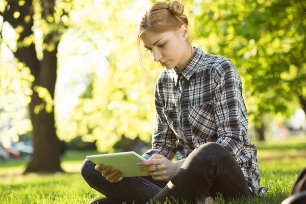 Young woman sitting on grass in park and using digital tablet — Stock Photo, Image