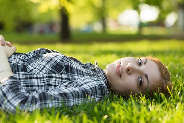 Young woman lying on grass in park and looking at camera — Stock Photo, Image