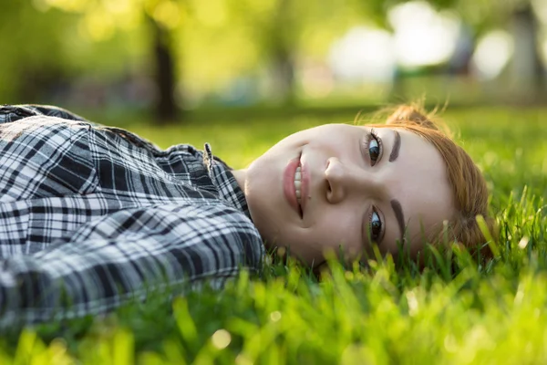 公園とカメラ目線で草の上に横たわる若い女性 — ストック写真