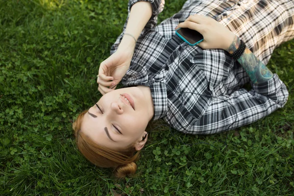 公園の芝生の上に横たわっている間音楽を聴く若い女性 — ストック写真