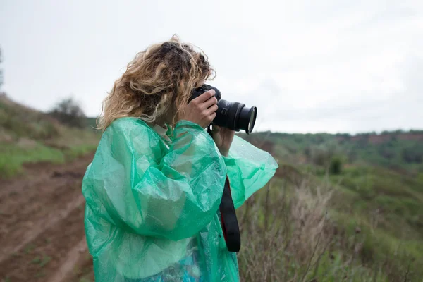 Mulher fotógrafa em capa de chuva tirar uma foto na paisagem da vida selvagem — Fotografia de Stock