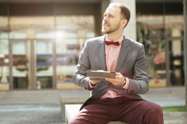 İşadamı şehir Avenue'de oturuyor ve uzağa bakarak dijital tablet kullanma