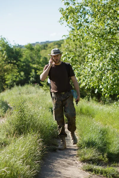 Turista masculino caminando en el bosque en el sendero y hablar por teléfono celular —  Fotos de Stock