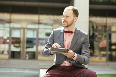 İşadamı şehir Avenue'de oturuyor ve uzağa bakarak dijital tablet kullanma