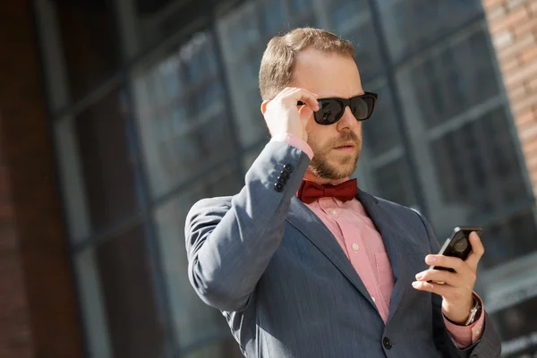 Elegante hombre de negocios en gafas de sol con teléfono inteligente en el centro de la ciudad —  Fotos de Stock