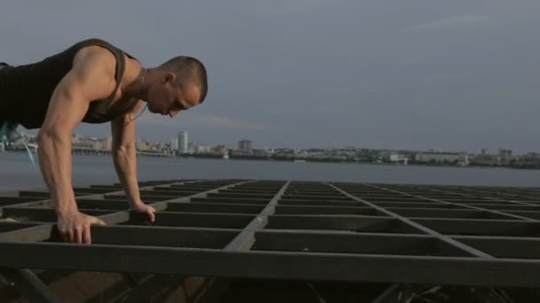 Hombre ejercitándose con flexiones en estructuras metálicas en el río — Vídeos de Stock