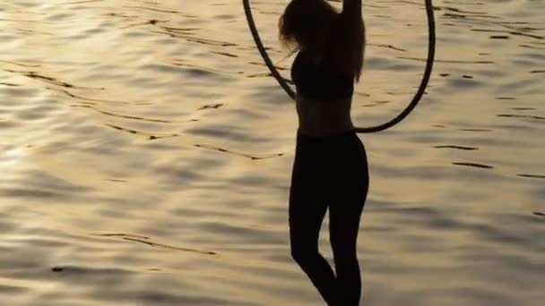 Silhouet van de vrouw zittend op grote stalen ring boven het water — Stockvideo