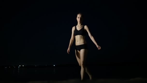 Flexible jeune femme faisant split sur fond noir à la plage de nuit — Video