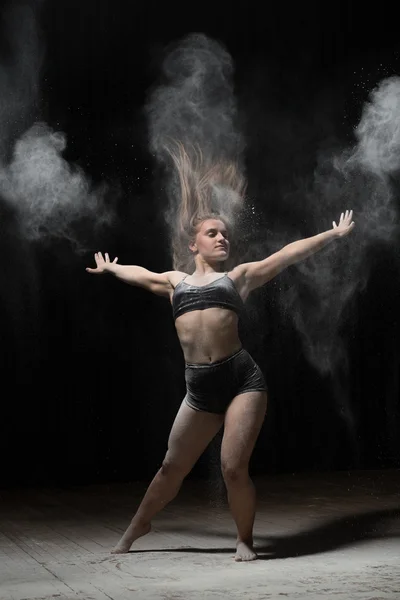 Bailarina joven bailando con harina sobre fondo negro — Foto de Stock