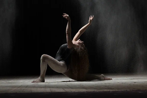 Flexible woman dancing with flour on black background — Stock Photo, Image