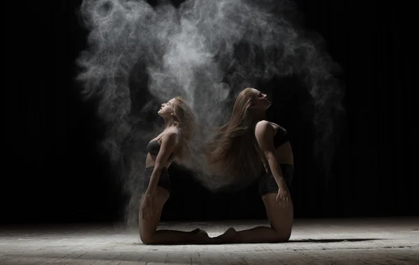 Dos bailarinas sentadas y espolvorean harina sobre fondo negro — Foto de Stock