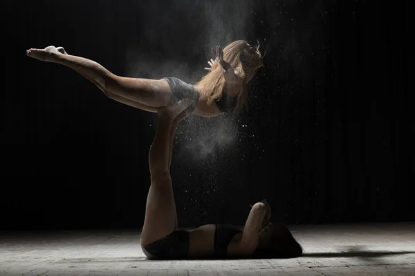 Two woman acrobatics posing and sprinkle flour on black background — Stock Photo, Image