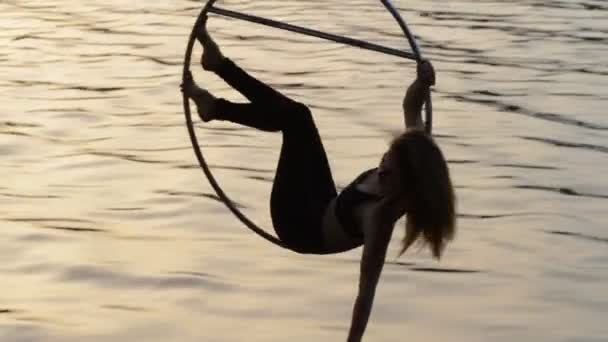 Silueta de mujer gimnasia de aire colgando en el aro aéreo por encima del agua — Vídeos de Stock