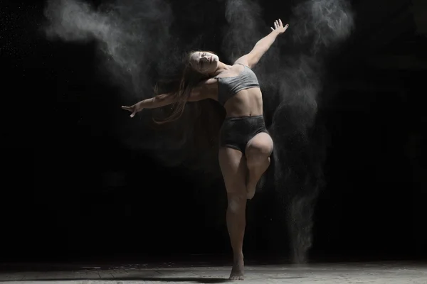 Mujer flexible bailando y espolvorear harina sobre fondo negro — Foto de Stock