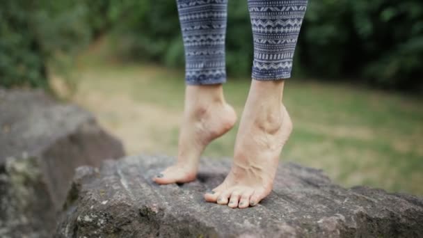 Женщина практикует йогу на большом камне. Ноги закрываются. . — стоковое видео