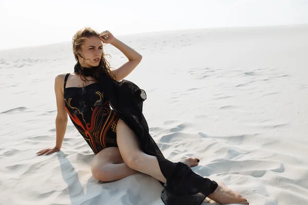 สาวสวยในชุดว่ายน้ํา นั่งบนทรายในทะเลทราย — ภาพถ่ายสต็อก