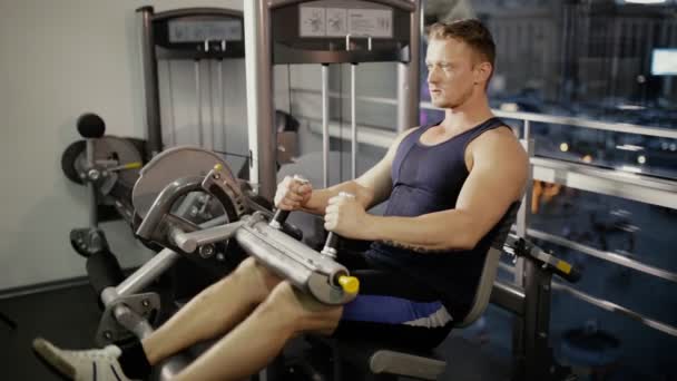 Чоловік накачує ногу на тренувальному апараті в спортзалі — стокове відео