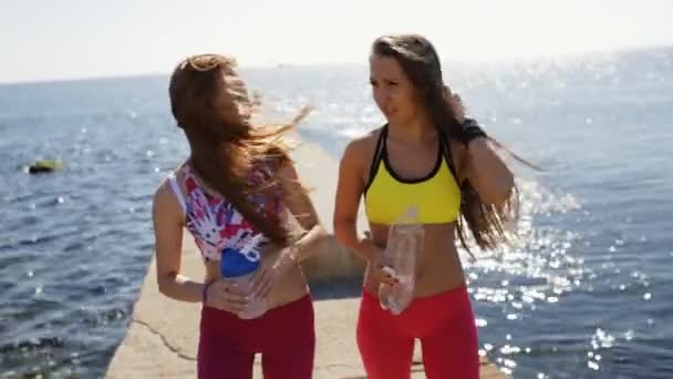 Sporty girlfriends drink water on sea pier after workout training — Stock Video