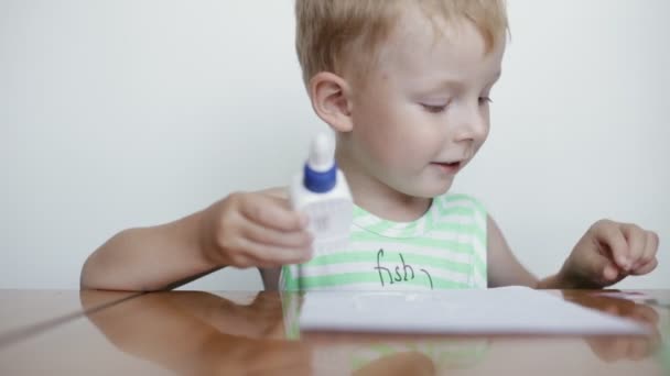 Pequeño niño pega papel sobre fondo blanco . — Vídeo de stock