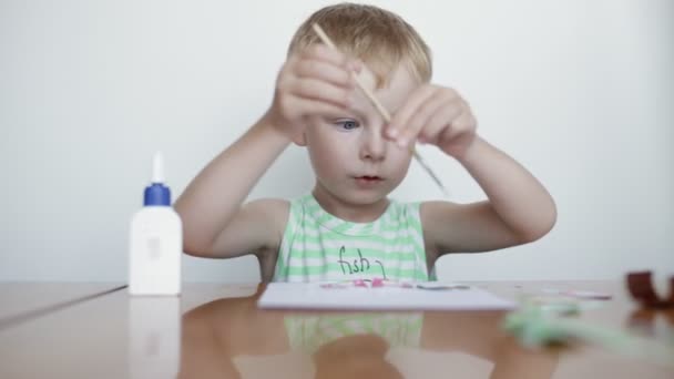 Pequeño niño pega papel sobre fondo blanco . — Vídeos de Stock