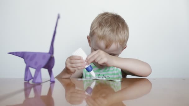 Дошкільна освіта. Маленький хлопчик клеїть папір на білому тлі . — стокове відео
