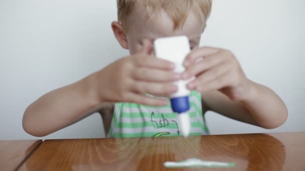 Förskoleundervisning. Liten pojke limmar papper på vit bakgrund. — Stockvideo