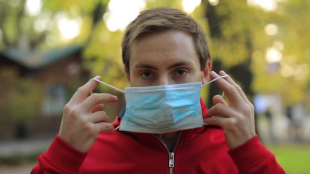 Een man draagt een chirurgisch masker in een park. — Stockvideo