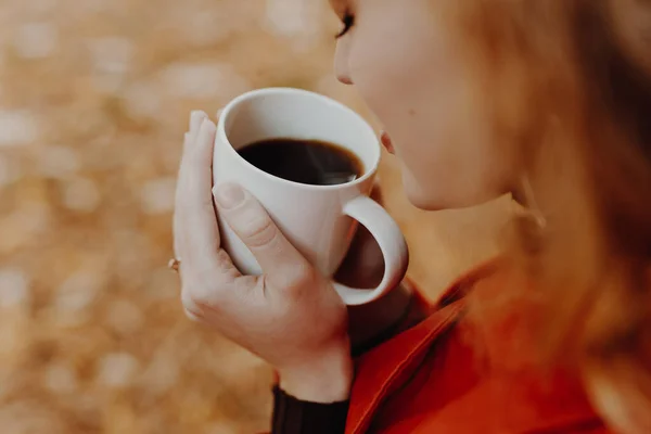 Woman sniff aroma of coffee at the fall day in park