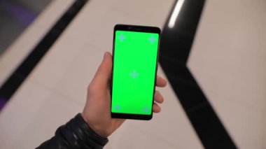 POV, alışveriş merkezinde yeşil ekranlı akıllı telefon kullanan bir erkek.