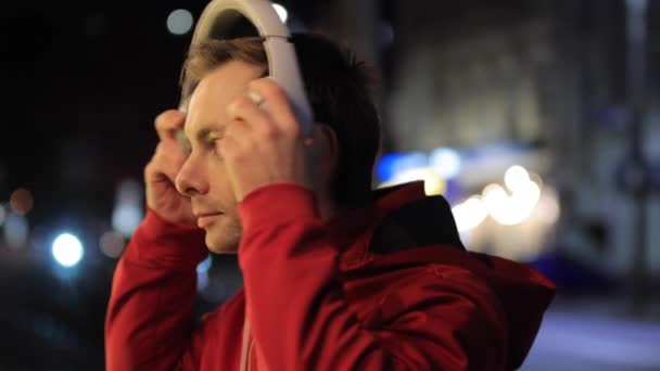 Homem usa fone de ouvido em uma cidade noturna — Vídeo de Stock