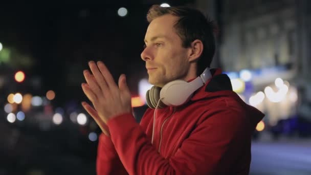 Homem congela à noite na cidade e aquece as mãos — Vídeo de Stock