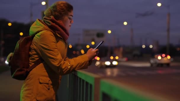 Kvinna med hjälp av telefon på natten stad nära vägtrafik — Stockvideo