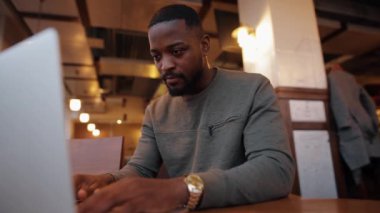 Bir kafede dizüstü bilgisayarla çalışan Afrikalı Amerikalı bir adam.