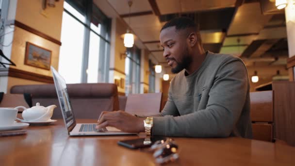 Africano americano homem on-line trabalhando por laptop em um café — Vídeo de Stock