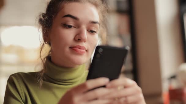 Młoda kobieta używa telefonu w kawiarni pijąc herbatę — Wideo stockowe