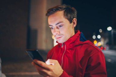 Kırmızılı adam gece cep telefonu kullanıyor.