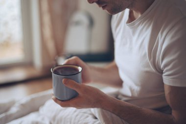Sabahları sıcak çay içen bir adam yatakta oturuyor.