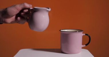 Turuncu arka planda pembe bir fincana süt dökmek