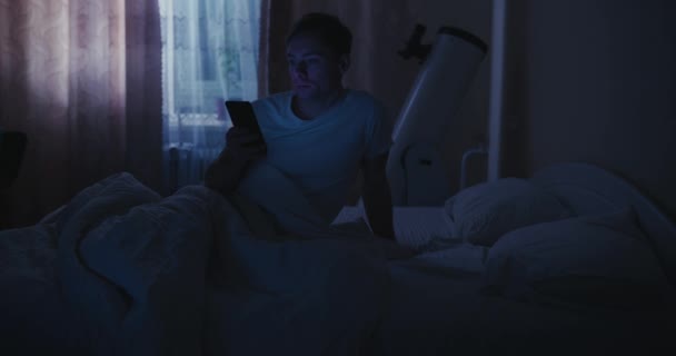 Hombre usando el teléfono móvil en la cama, luz azul — Vídeos de Stock