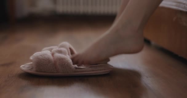 Женские ноги встают с кровати и надевают домашние тапочки — стоковое видео