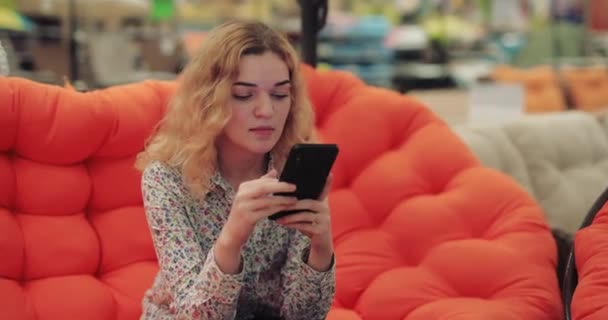 Coquette γυναίκα χρησιμοποιώντας smartphone κάθεται σε πορτοκαλί καναπέ — Αρχείο Βίντεο