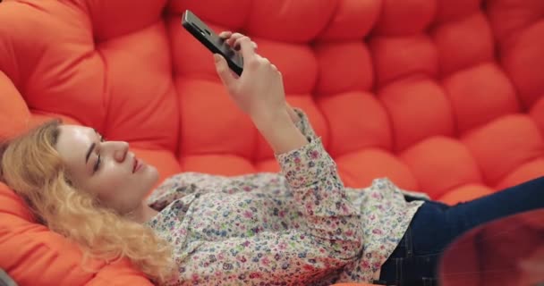 Vrouw met smartphone zittend op oranje bank — Stockvideo