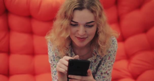 Vrouw met smartphone zittend op oranje bank — Stockvideo