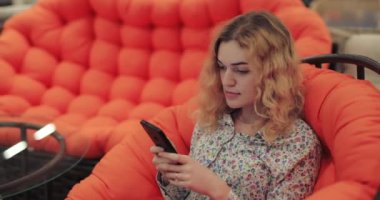 Turuncu koltukta oturan akıllı telefon kullanan bir kadın.